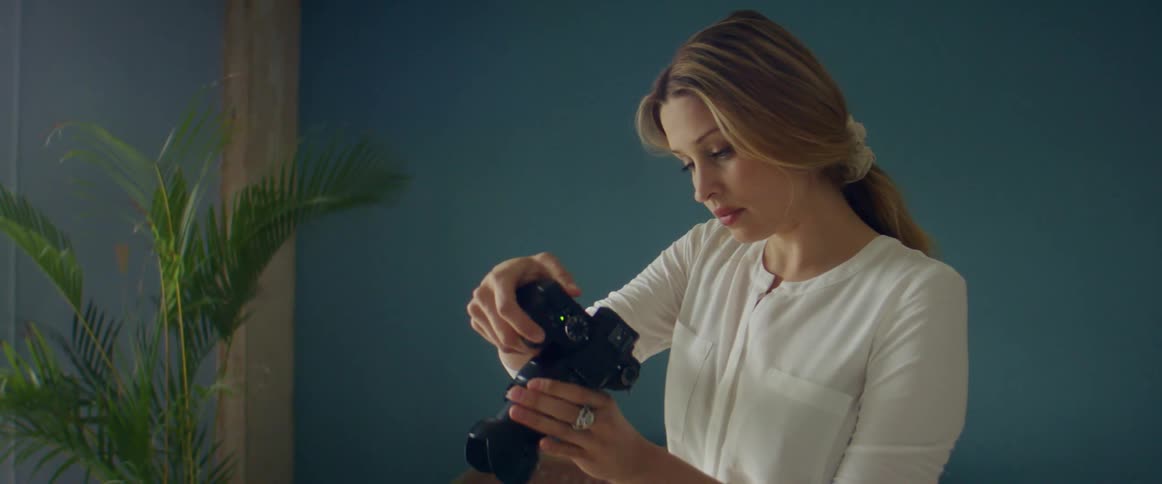 A woman is standing indoors and holding a camera