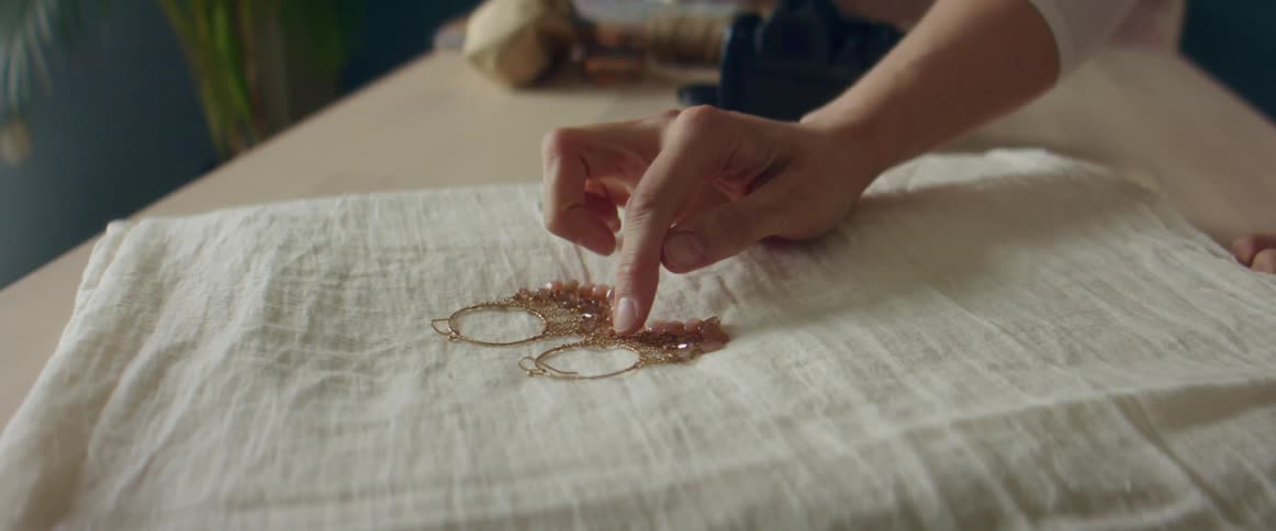 A woman takes a photo of beaded gold hoop earrings placed against a white linen cloth
