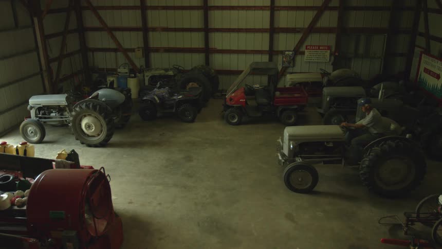 A man walks into an equipment barn and drives a small tractor out