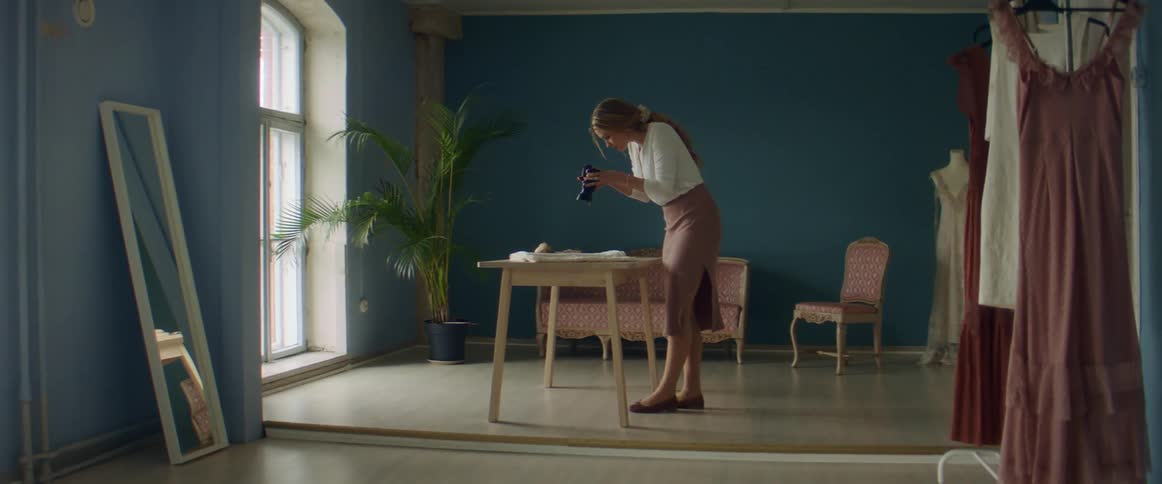 A woman in a room using a camera with a wall and window in the background