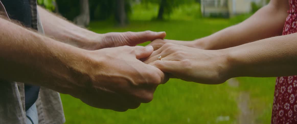 An engaged couple hold hands as they stand in their front yard