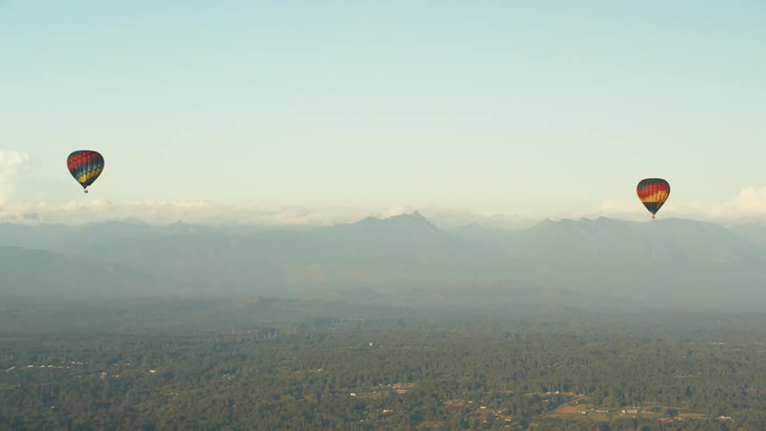 Hot air balloons floating in the air over a landscape with a mountain range the sky and clouds in the background