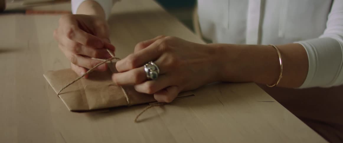A woman ties twine around a small package wrapped with butcher paper