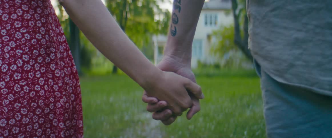 Couple walks hand in hand across green lawn toward large white house