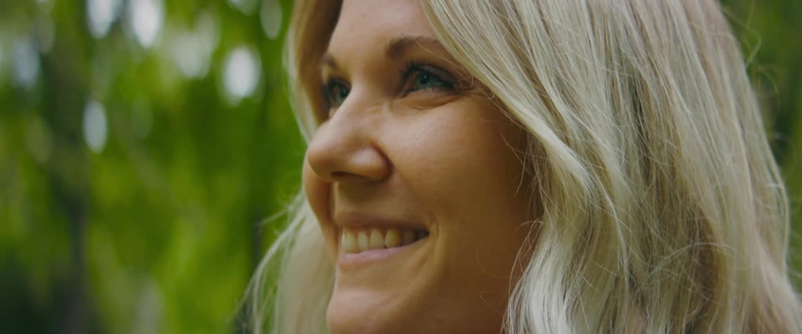 Close up of a smiling blonde woman standing near the trees