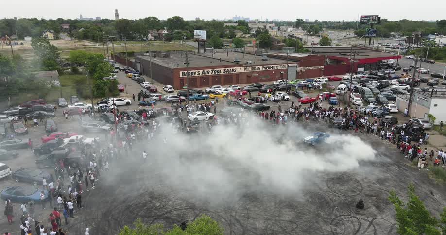 A vehicle does donuts in a parking lot with a large crowd of spectators