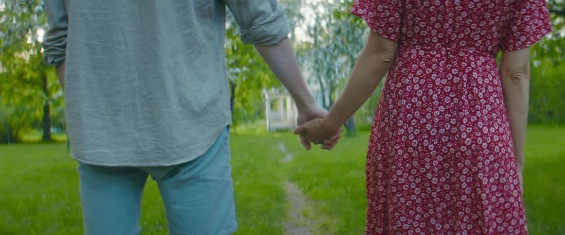 A man and woman walk through a field while holding hands during the day