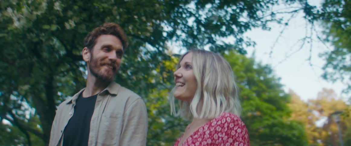 A couple laugh as they walk in the park and stop underneath a tree to kiss