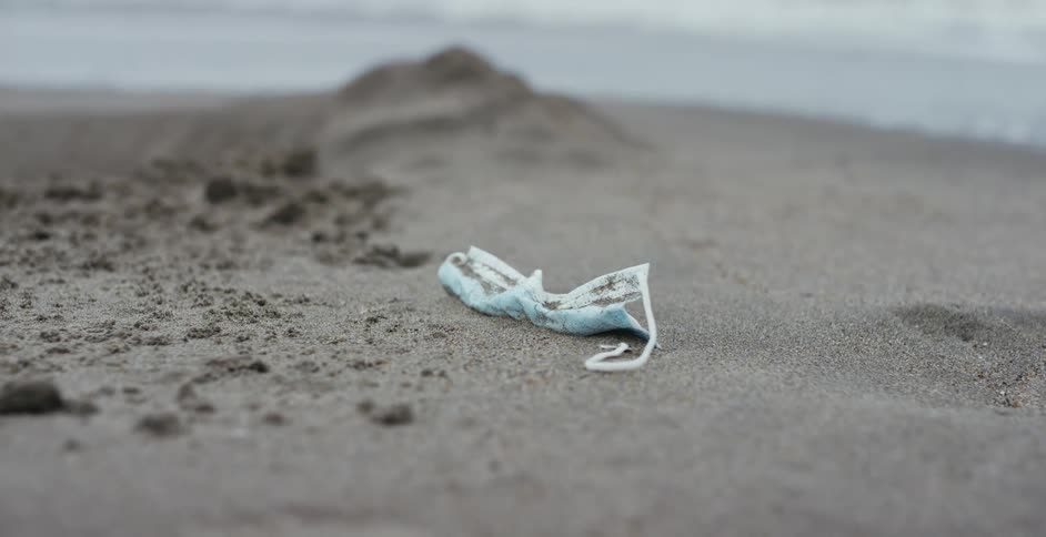 Blue face mask thrown over the sand of a beach next to the ocean
