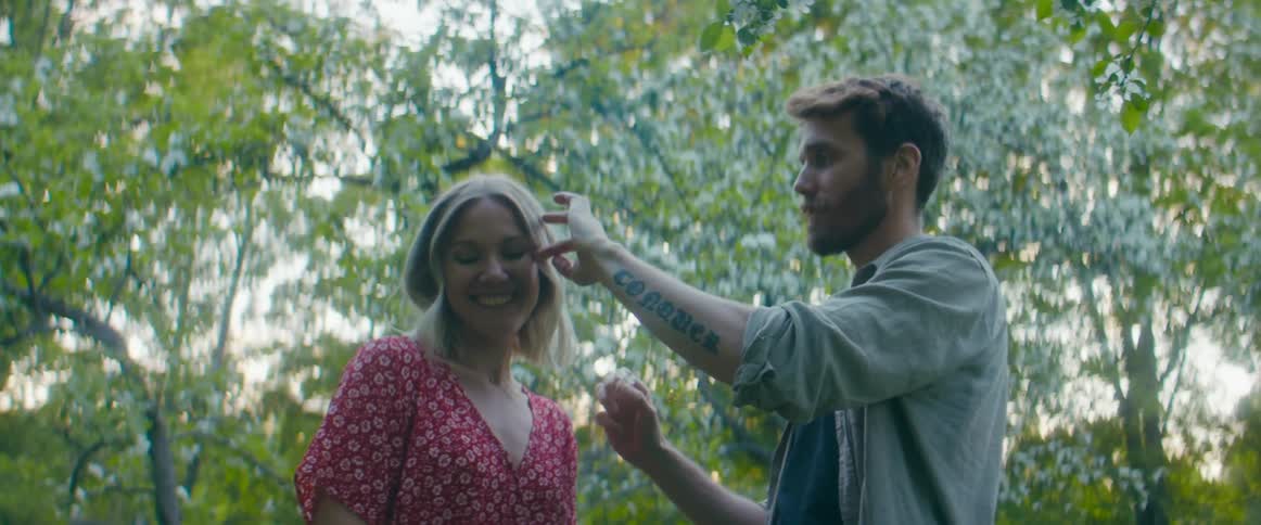 Man plucks flowers from flowering tree and places it behind smiling womans ear