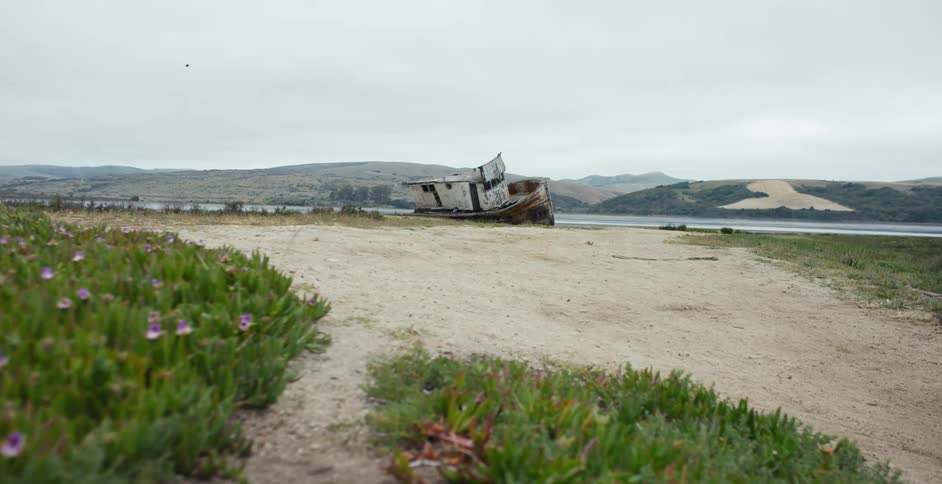A shipwrecked boat sits on the coast of a small beach Point Reyes, California