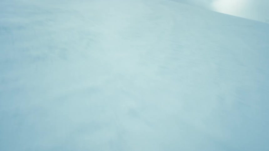 A field covered in snow blowing behind a snowboarder