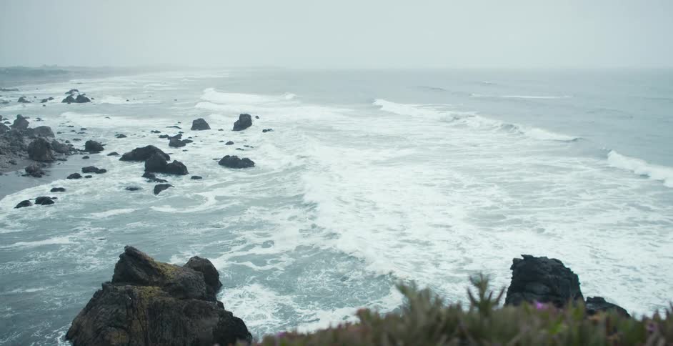 Ocean waves crashing on the black rocks on the cliffs of a beach