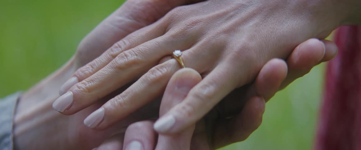 A man slides an engagement ring onto the finger of a woman