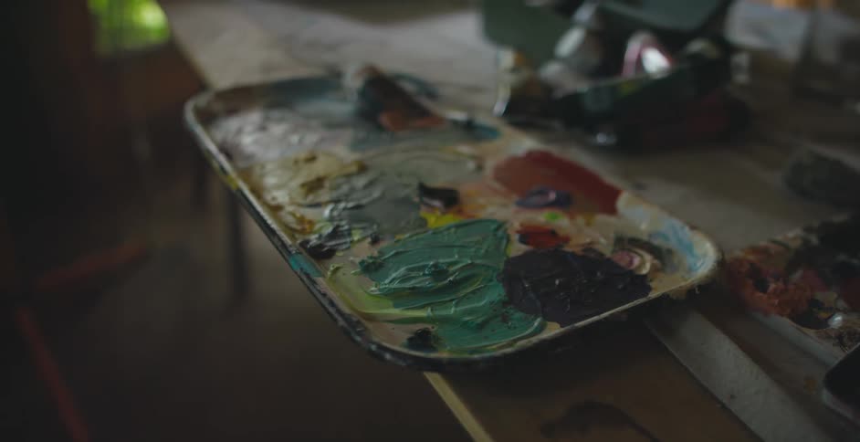 A rectangular tray that has artists paint on it sits at the edge of a table