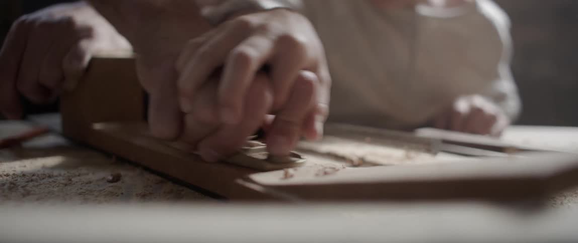 An adult teaching a child how to use a wood shaving tool