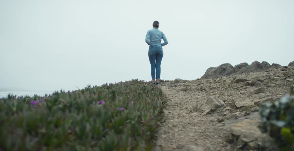 A woman stands on the coast and looks out at the water
