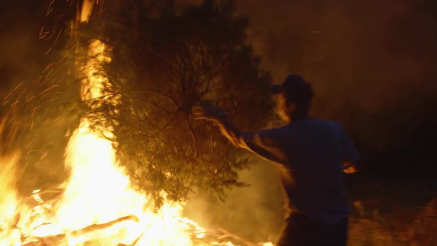 A man with a hat throwing a tree onto a fire with smoke