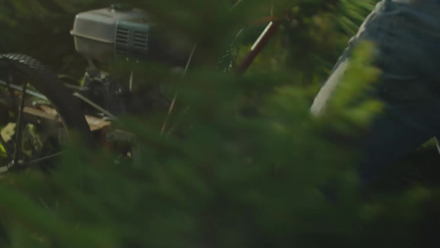 A man pushing a lawnmower surrounded by plants and trees