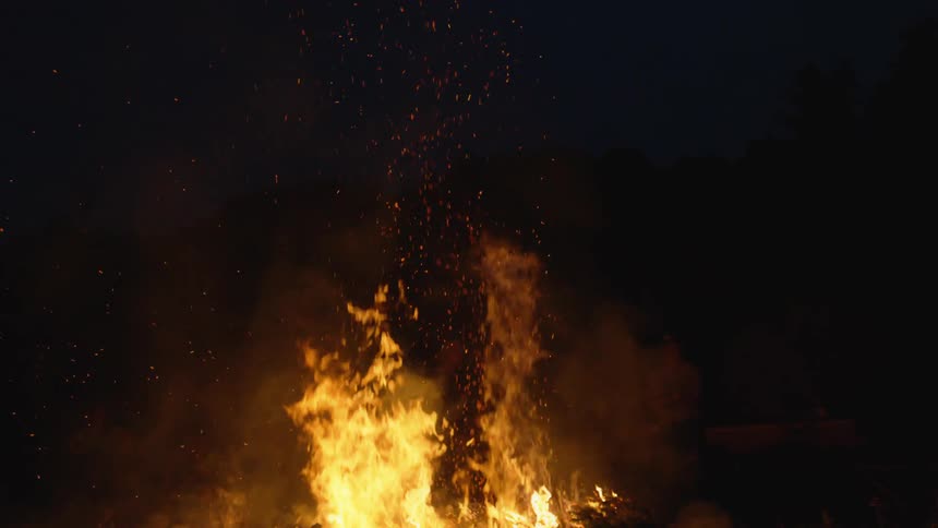 A large bonfire sends embers into the night sky