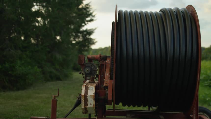 A machine rolling out a hose with trees the sky and clouds in the background