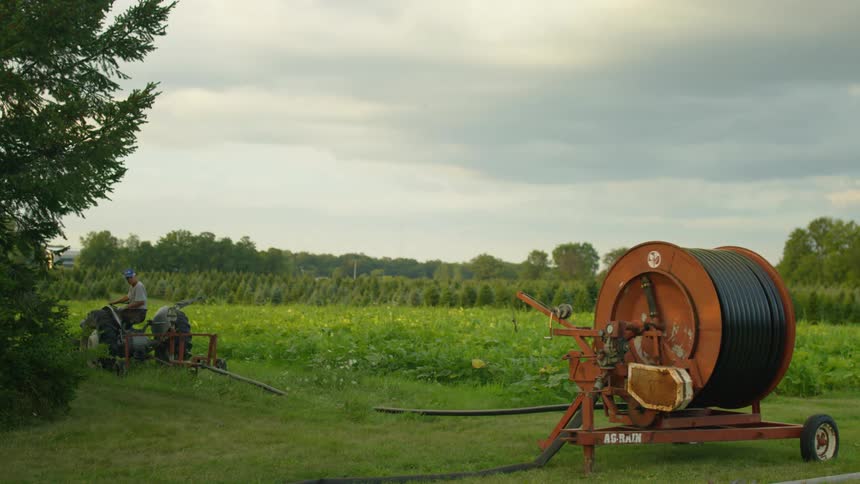 A person drives a tractor in a field pulling a large cable behind it
