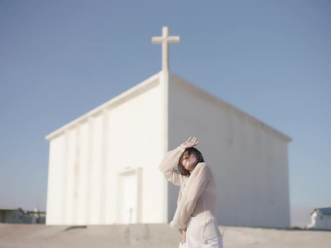 A woman dances in front of a rural white church building