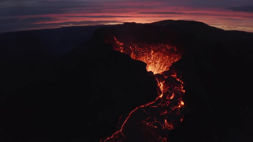 Lava flowing from the crater of a volcanic vent silhouetted against the sunset