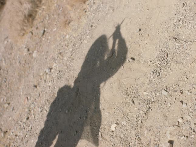 A woman casts a shadow on the ground as she stretches while backpacking through the desert