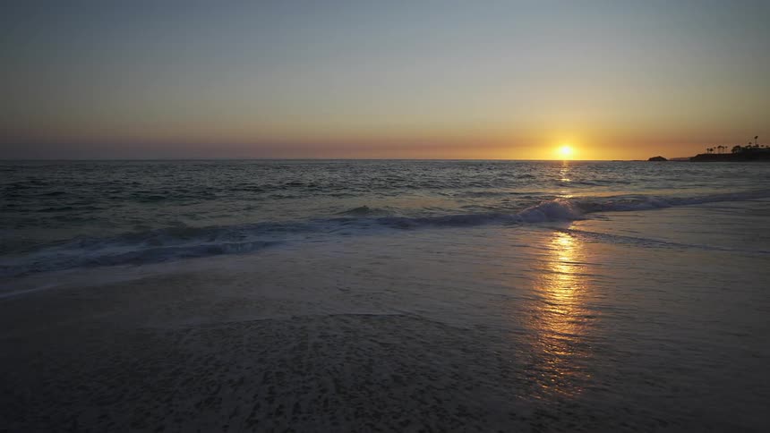 Ocean waves roll in over a beach with a sunset on the horizon