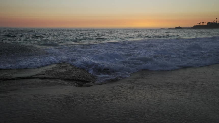 Ocean waves curl and splash on shore at sunrise with palm tree silhouettes behind