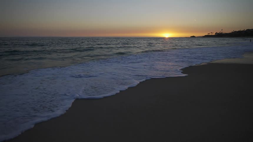 Ocean waves roll in over a beach with a sunset on the horizon