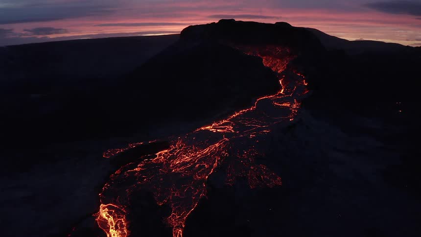 Lava on the slope of a volcano glows from heat in the darkness of sunset