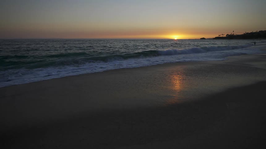 Ocean waves roll in over a beach with a sunset on the horizon