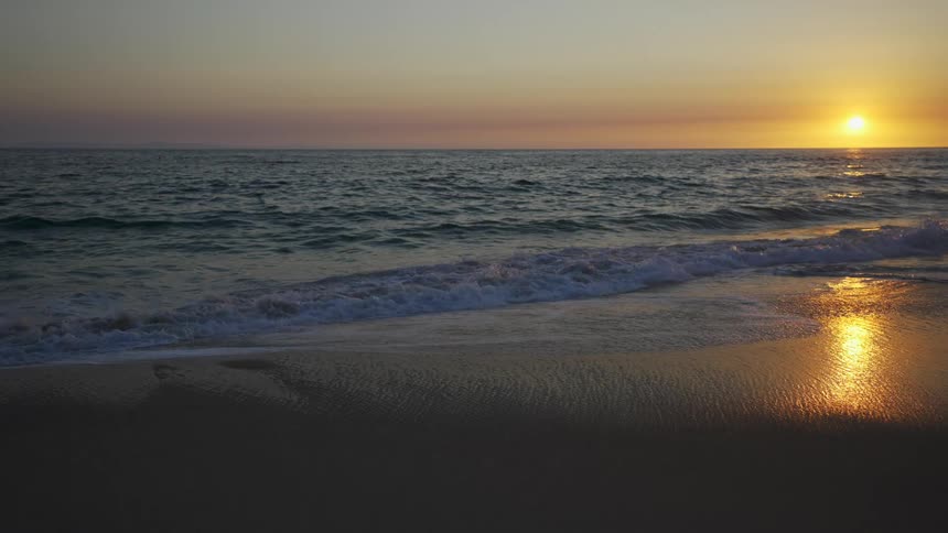 The sun glows yellow and reflects on the ocean waves and wet beach sand