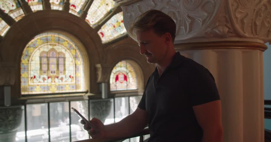 Man standing inside a building with classical architecture texting on his phone