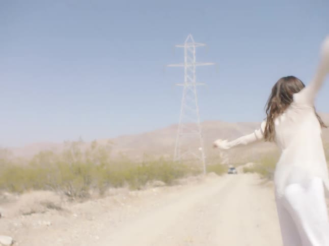 A woman dances and twirls on a desert dirt road