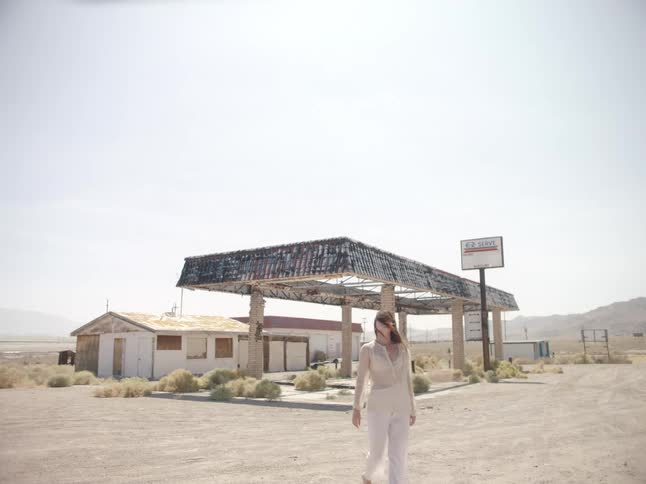 Woman wearing white clothes walking near an abandoned gas station in the desert