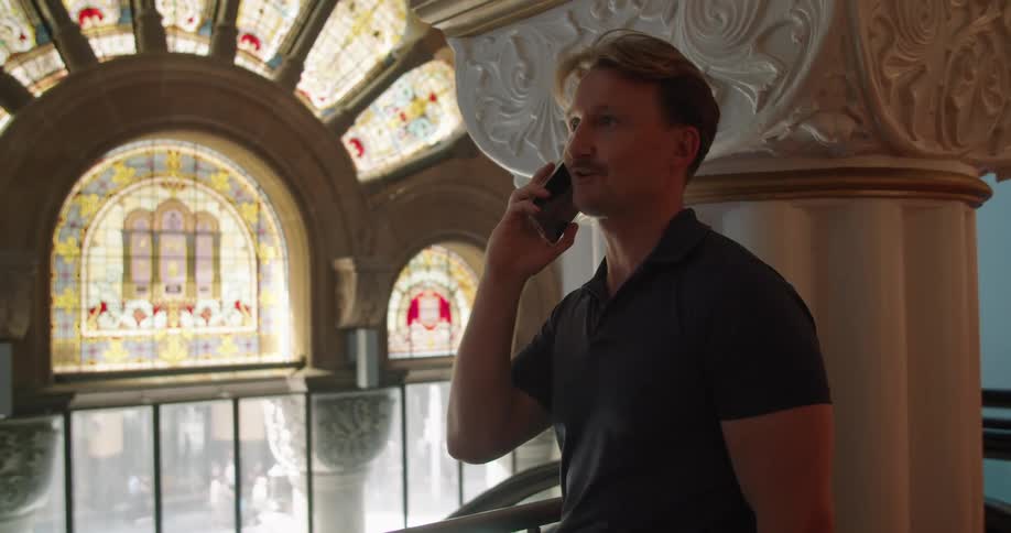 A man in a building answers his cell phone as people walk on the street outside