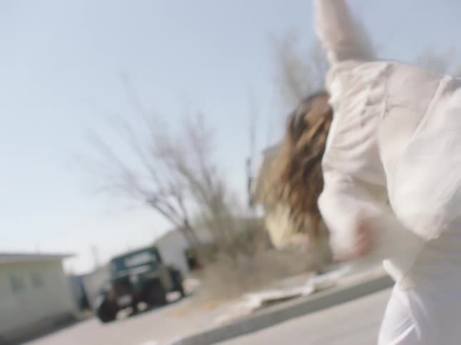 A woman dancing on the street with houses the sky and clouds in the background