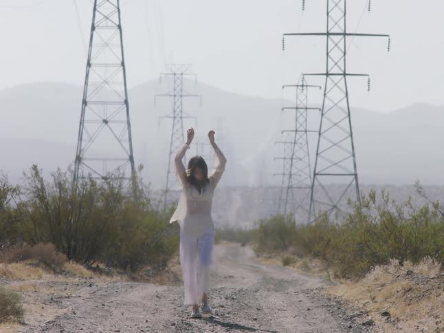 A woman wearing all white walks along a remote dirt road