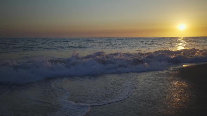 Sun nears horizon turning sky red and reflects of ocean as waves crest onto shadowed beach