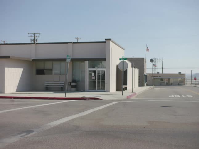 A building at an empty intersection with a bench in front and an american flag flying