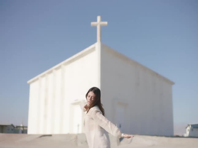 Woman wearing white clothes dancing in front fo a church in the countryside