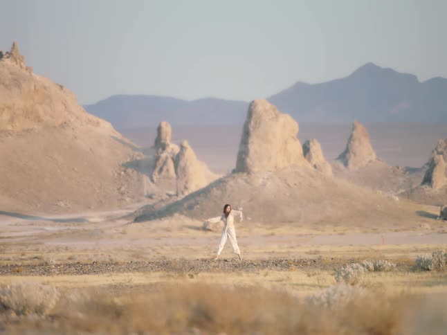 A woman dances and twirls in the desert as the wind blows her hair and clothing
