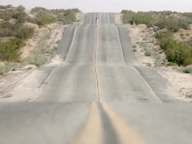 Wide shot of a person walking on a deserted undulated road