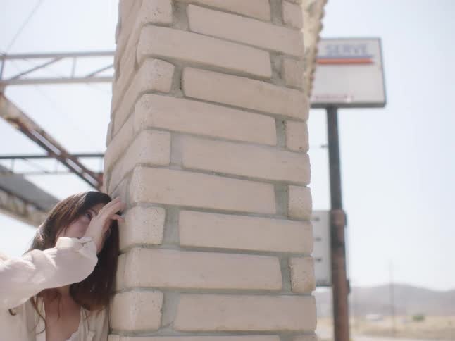 Woman leans against column reaching her hand higher and higher against the bricks with mountains on horizon