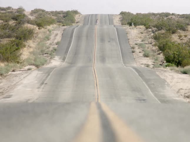 A person walking down a road in the middle of the desert