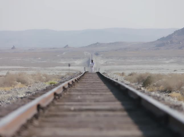 A woman is seen walking on empty train tracks at a distance