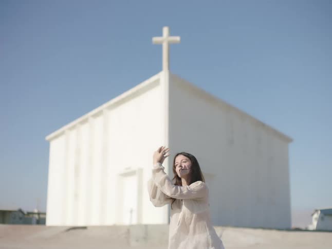 A woman dancing with a church the sky and clouds in the background